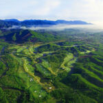 An elevated view of the course, which is bordered by foliage covered hills