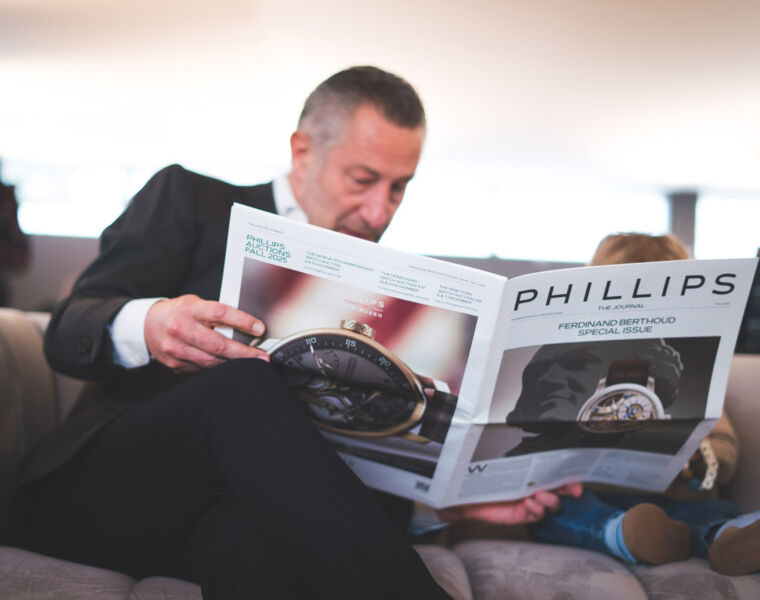 Phillips’ Decade One Auction Sees New World Records and 100% of Lots Sold 13 A man sitting on a sofa browsing the auction catalogue